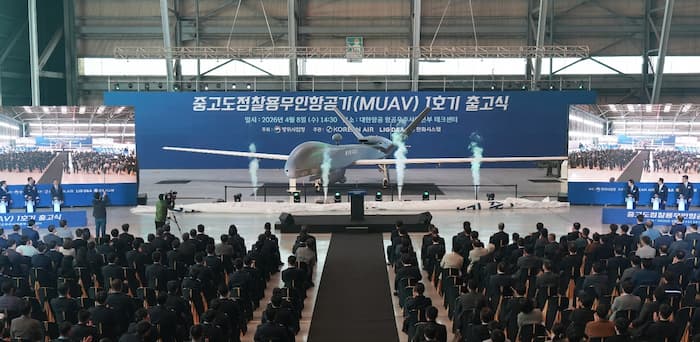 격납고 무대 중앙에 전시된 중고도 무인기(MUAV) 1호기와 이를 지켜보는 수백 명의 참석자들.