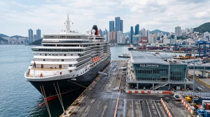 A large cruise ship docked at a modern Korean port terminal with a city skyline and harbor facilities in the background