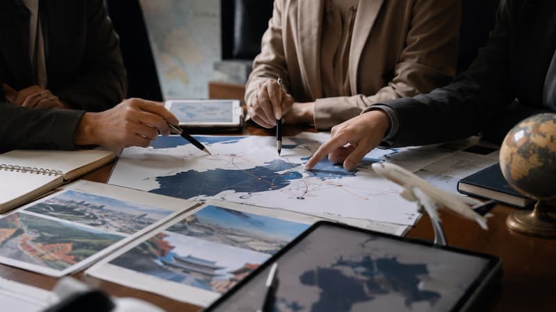 Hands pointing to a market planning map with travel documents and an aircraft model on the table