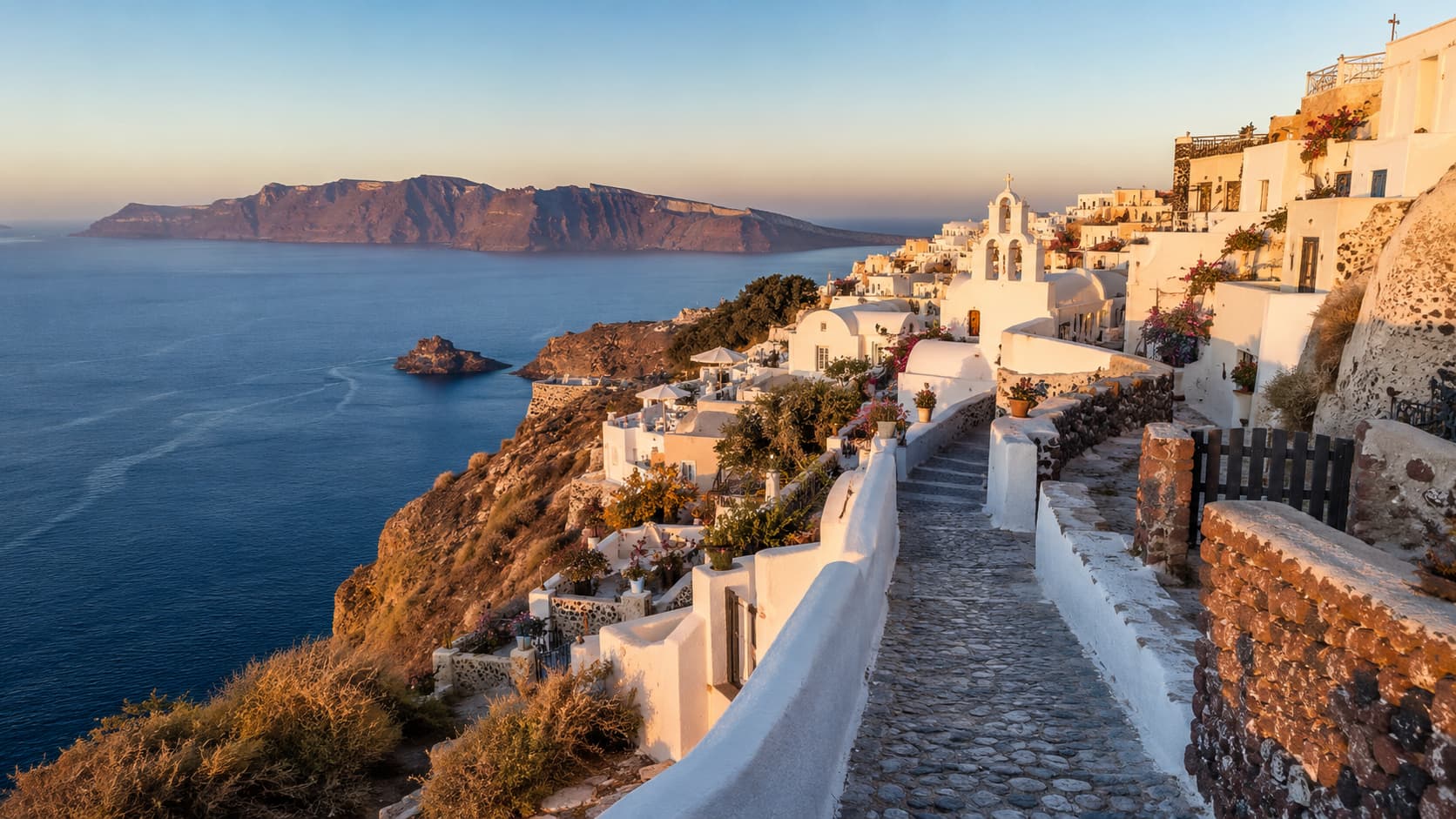 A walking path through a whitewashed Santorini village overlooking the caldera and the Aegean Sea