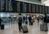 국제공항 출발 안내판 아래에서 항공편을 확인하는 여행객들